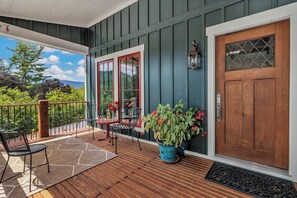 A wooden deck with a table and chairs, a potted plant, and a door with a window. - Cozy Craftsmen (Black Mountain)