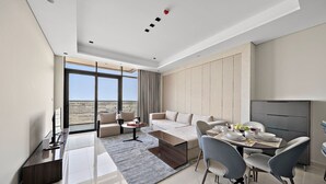 Een moderne hotelkamer met een groot raam, een zithoek, een eettafel met stoelen en een flatscreen televisie.