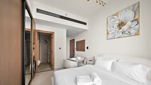 Una habitación de hotel moderna con una cama grande, un baño con ducha, una mesita pequeña y un espejo.