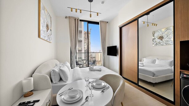 Una habitación de hotel moderna con balcón, un comedor con mesa redonda y un espejo grande que refleja la habitación.