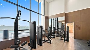 Un gimnasio moderno con diversas máquinas de ejercicio, amplias ventanas y vistas a la ciudad.