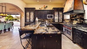 A modern kitchen with dark cabinetry, a granite countertop, and a central island. - 5BR Golf Villa- Airport Trans Included (Cabo San Lucas)