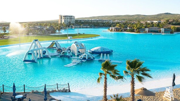 A resort with a large swimming pool, palm trees, and a view of distant buildings. - 5BR Golf Villa- Airport Trans Included (Cabo San Lucas)