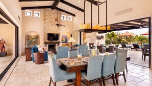 A spacious living area with a stone fireplace, a dining table set for six, and a large TV screen. - 5BR Golf Villa- Airport Trans Included (Cabo San Lucas)