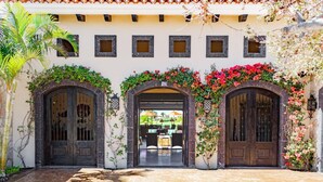 A courtyard with two wooden doors, a covered patio area, and a building with a tiled roof. - 5BR Golf Villa- Airport Trans Included (Cabo San Lucas)