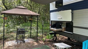Een camper met een barbecue en een tafel onder een beschaduwd gebied.