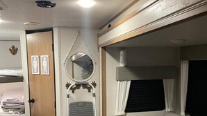 Een compact camperinterieur met een bed, een zithoek, een opbergruimte en een klein raam.