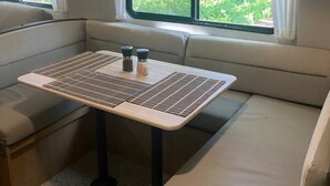 Een gezellig RV-interieur met een zachte zithoek, een klein tafeltje met zout- en peperstel, en een raam met uitzicht op groen.