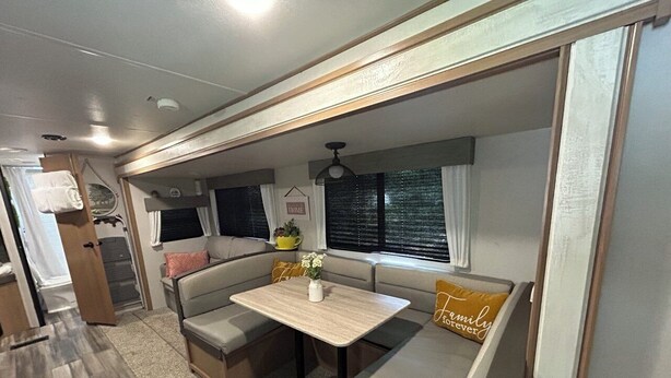 Een compact camperinterieur met een eethoek, een kitchenette en een zithoek met een kussen met de tekst 'Family Forever'.