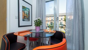 A modern room with a glass table, two orange chairs, a potted plant, and a framed picture on the wall. - Wakefield Westgate Station - 2 Bed 2 Bath (Wakefield)