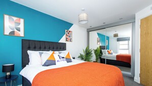A modern bedroom with a large bed, a nightstand, a mirror, and a potted plant. - Wakefield Westgate Station - 2 Bed 2 Bath (Wakefield)