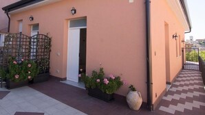 Un bâtiment à la façade de couleur pêche, doté d’une entrée fermée par un portail et agrémenté de plantes en pot ornées de fleurs roses.