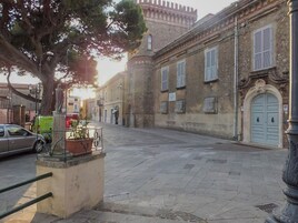 Una calle tranquila con edificios históricos, una estatua y un coche aparcado al borde.