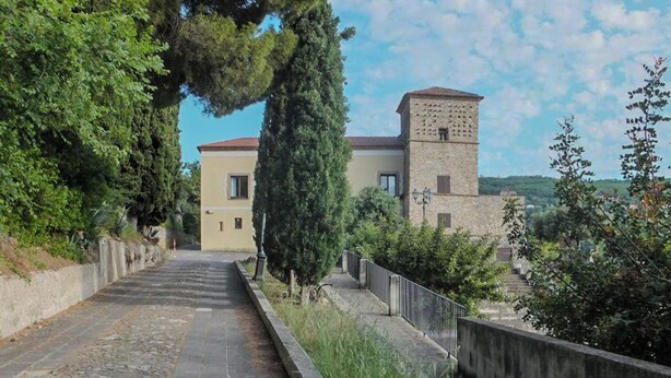 Un chemin menant à un bâtiment doté d’une tour, entouré de verdure.