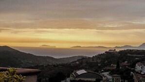 Une ville côtière au coucher du soleil, avec des bâtiments sur une colline et une vue dégagée sur la mer.