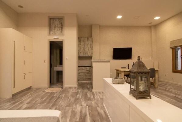 A modern kitchen with a flat-screen TV, a dining area with a table and chairs, and a hallway leading to another room.