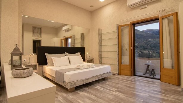 A bedroom with a large bed, a bedside table, a nightstand, a mirror, and a view of the outdoors through a sliding glass door.