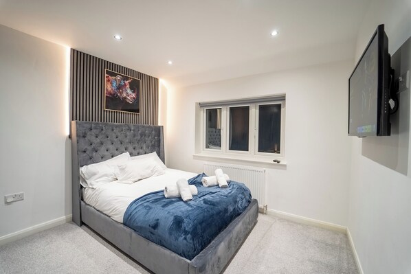 A modern bedroom with a grey tufted headboard, white bedding, and a blue accent bedspread. - Luxury Retreat, Hot tub, SuperKing Massage Bed, Tesla
Warner bros, Contractors! (Northwood)