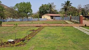 A grassy area with a small building, a paved path, and a blue fence.
