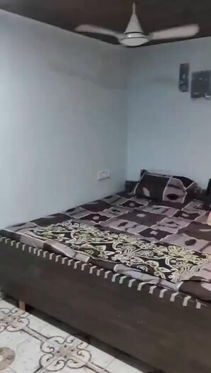 A bedroom with a bed, a ceiling fan, and a wall socket. - BapuJi Ni Wadi (Panvel)