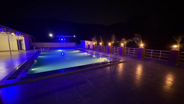 A swimming pool with a tiled deck, surrounded by a low fence and palm trees.