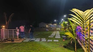 A nighttime outdoor area with a paved path, palm trees, and string lights.