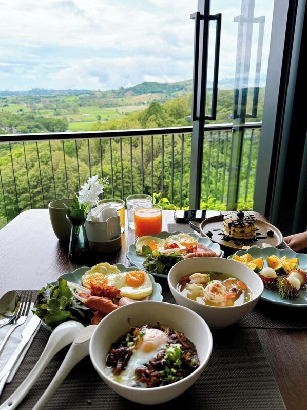 A dining table with breakfast dishes, a glass of orange juice, and a scenic view through a balcony. - Kiri Rhom Khao Kho (Khao Kho)