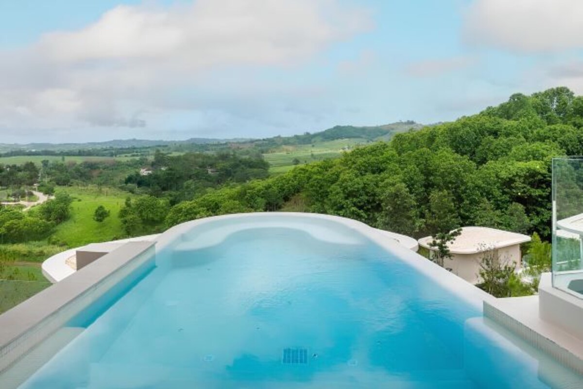Una piscina infinita moderna con vistas despejadas a un paisaje verde exuberante y colinas al fondo.