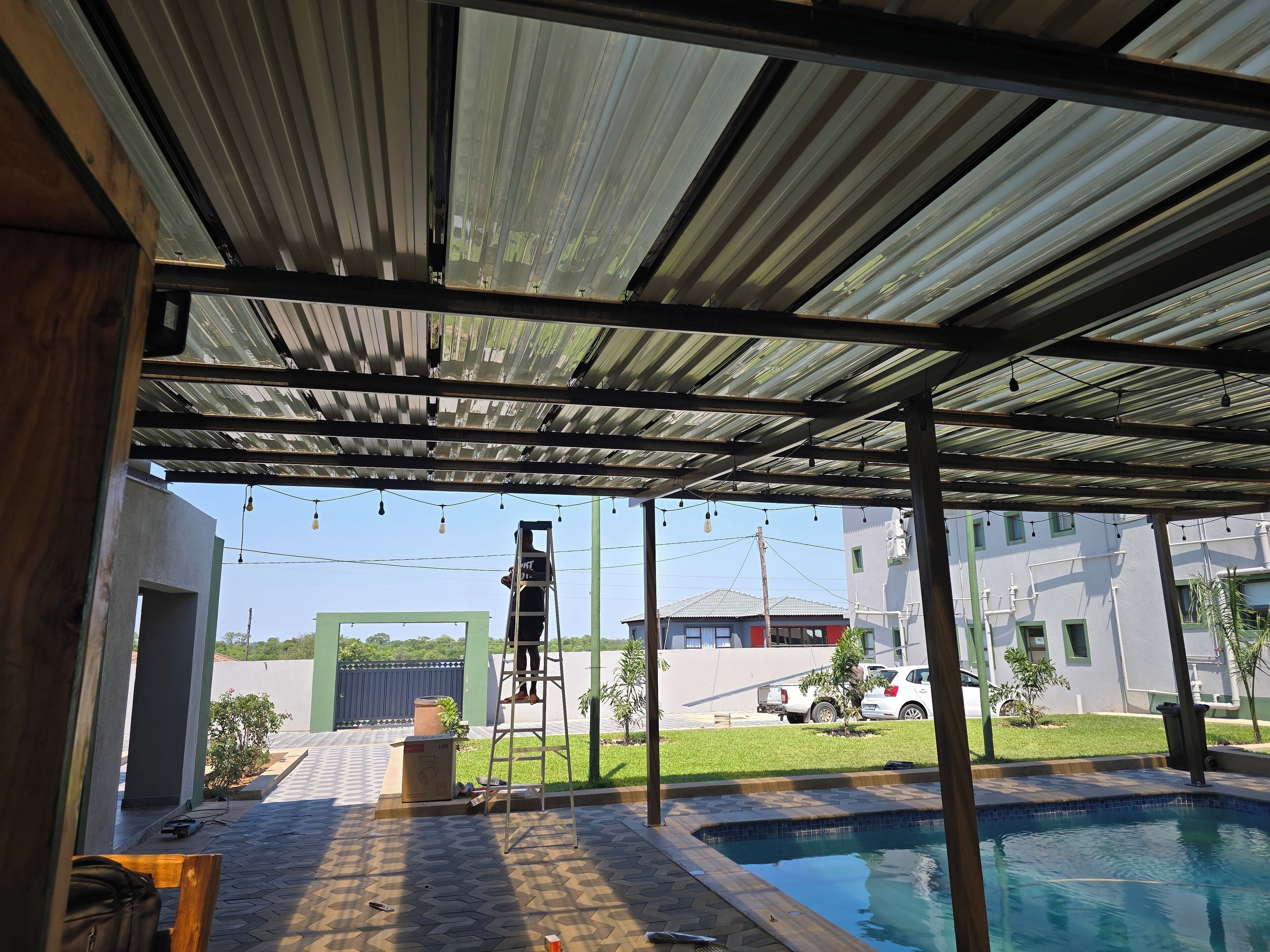 A covered outdoor area with a pool, a ladder, and a person on a ladder.