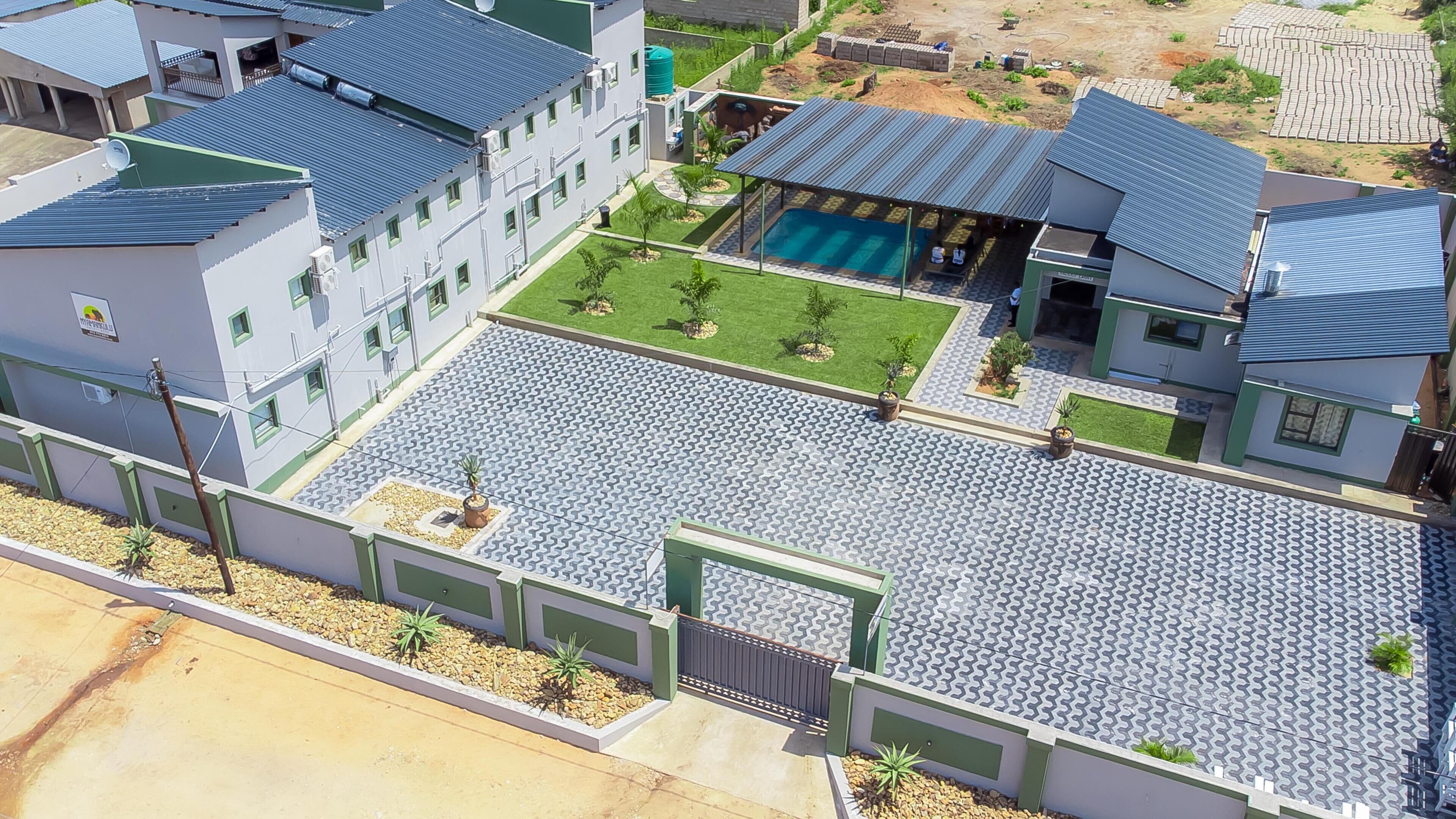 A modern building with a swimming pool, green lawns, and a paved courtyard.