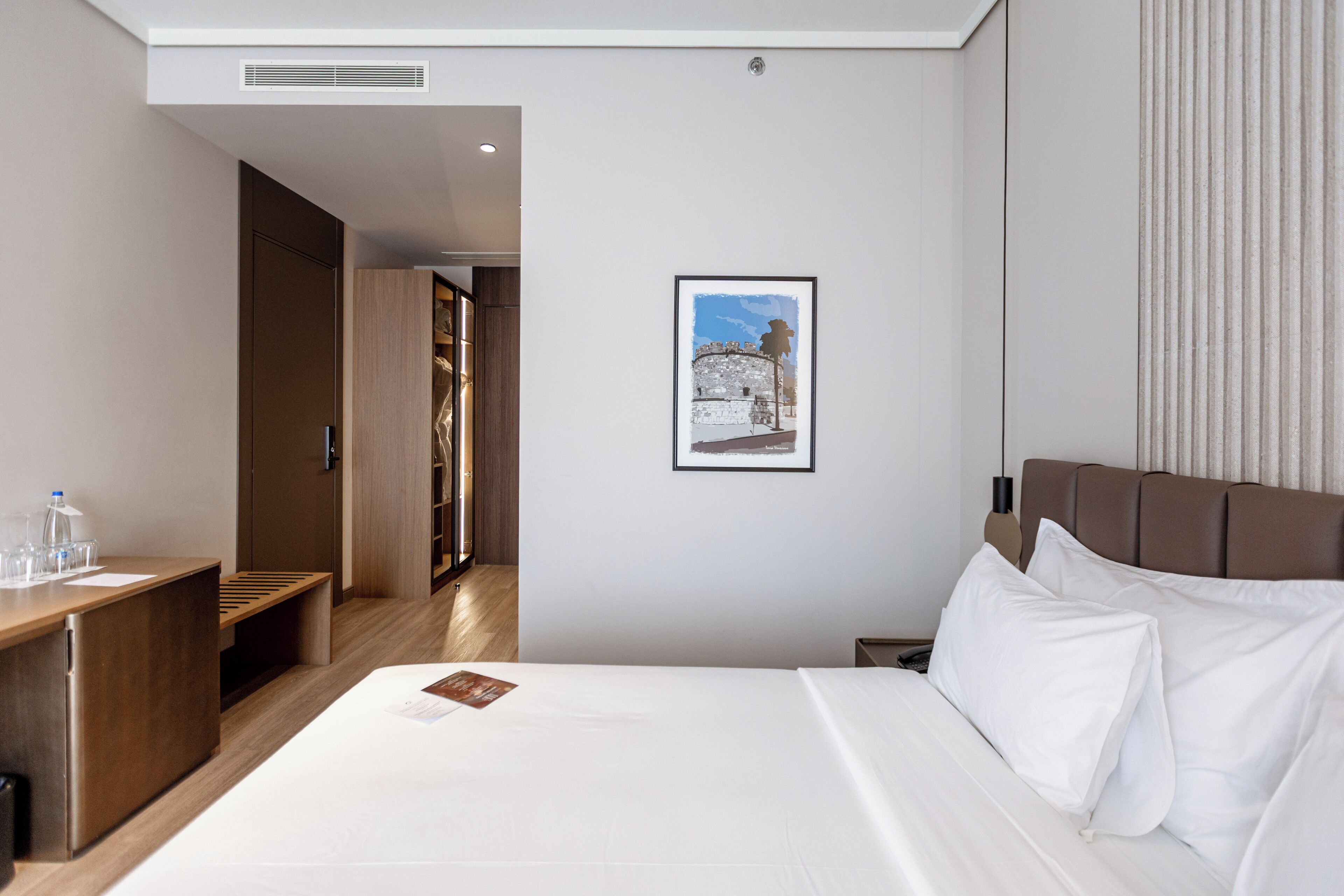A hotel room with a bed, bedside table, and a framed picture on the wall.