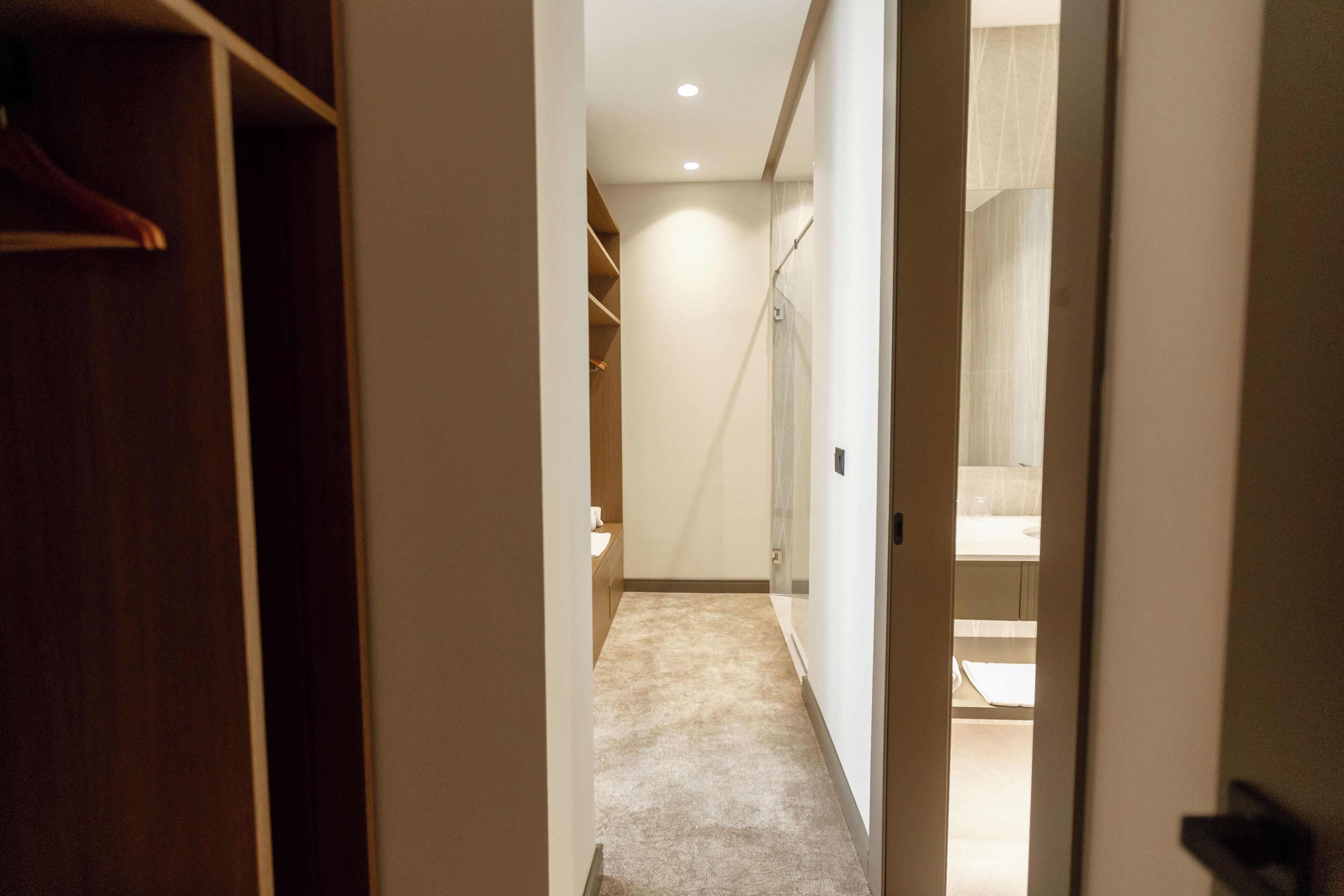 A hallway leading to a bathroom with a shower, a toilet, and a sink.