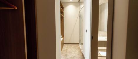 A hallway leading to a bathroom with a shower, a toilet, and a sink.