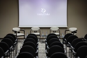 A conference room with rows of chairs facing a projector screen displaying 'Grand Duka Hotel & SPA' logo. - Grand Duka Hotel & Spa (Durrës)