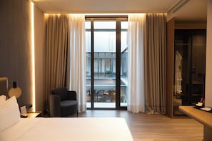 A hotel room with a large bed, a chair, a desk, and a sliding glass door leading to a balcony. - Grand Duka Hotel & Spa (Durrës)