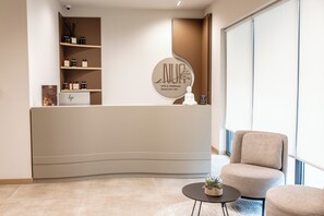 A reception desk with a sign reading 'NUR Spa & Wellness Retreat Into Calm,' a small Buddha statue, and a potted plant on a round table. - Grand Duka Hotel & Spa (Durrës)