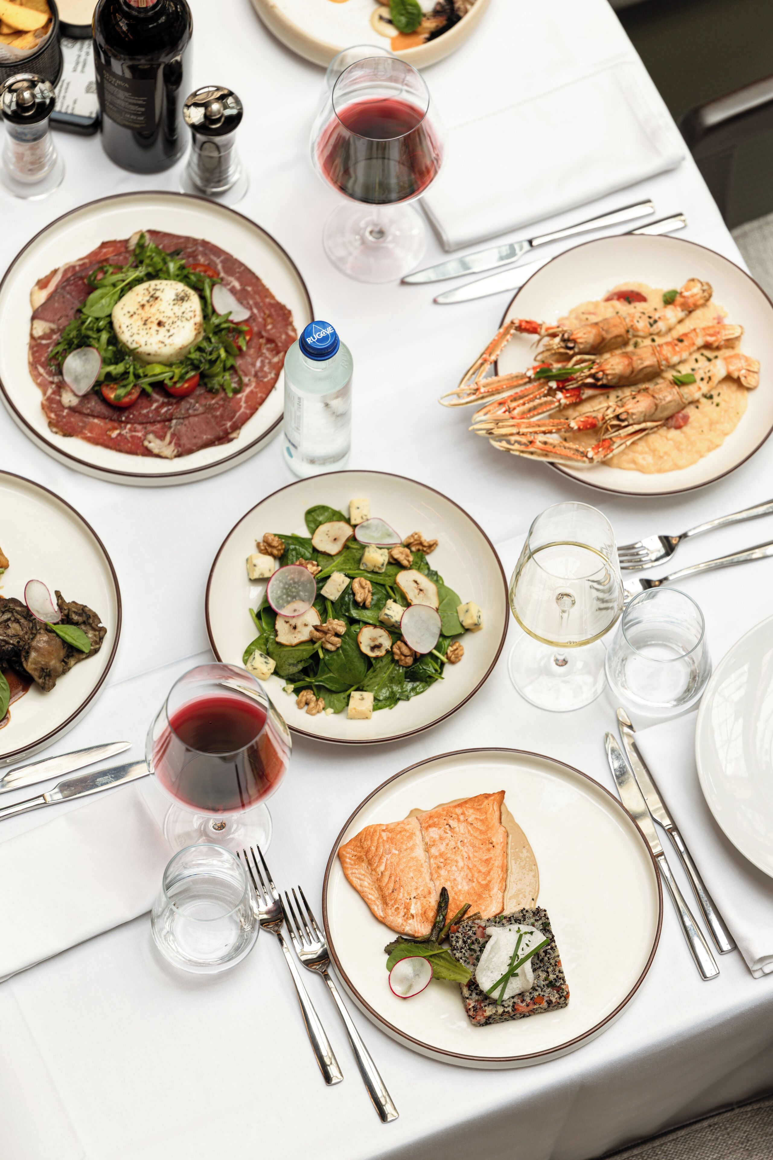 Une table dressée avec différents plats, des verres de vin rouge et des couverts.