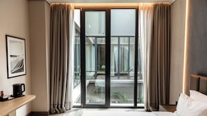 Ein Hotelzimmer mit einem großen Bett, einem Schreibtisch mit Kaffeemaschine und Blick auf einen Balkon mit Pflanzen.