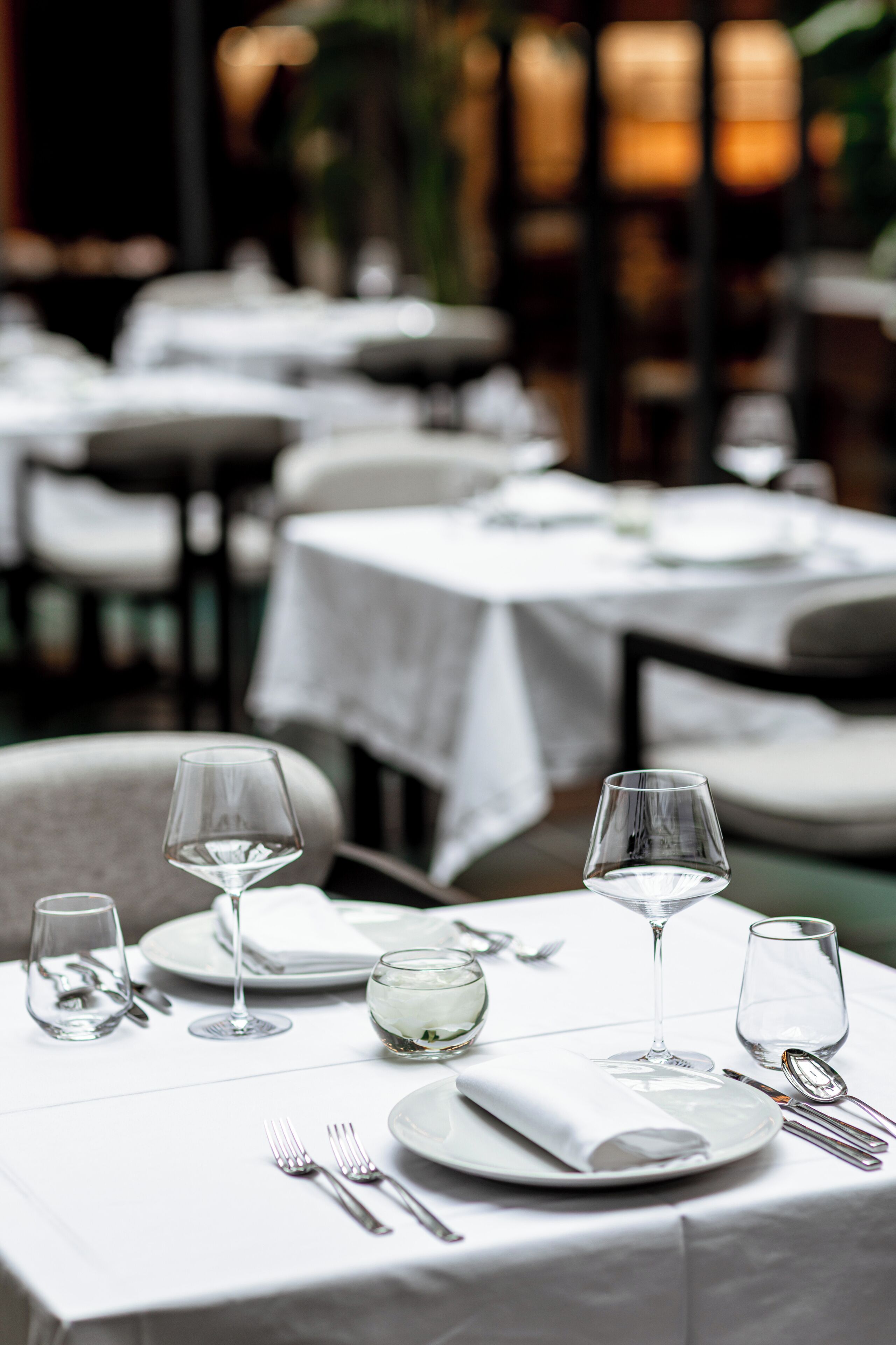 Un ambiente de restaurante con mesas dispuestas para comer, con manteles blancos y copas de cristal.