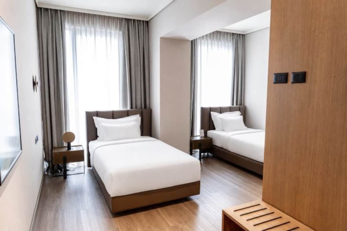 Una camera d'albergo con due letti, una panca di legno e uno specchio grande.