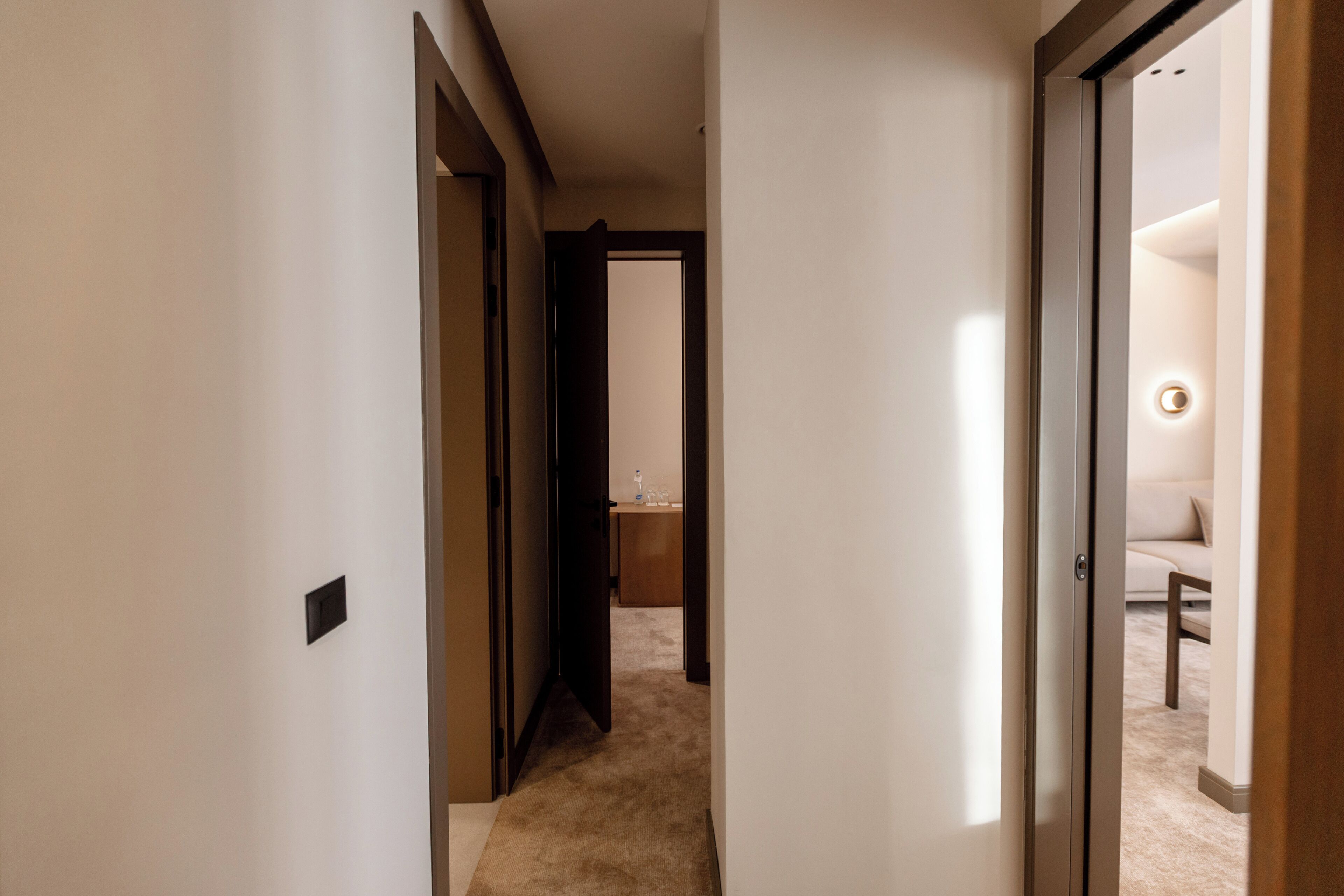 Un pasillo que conduce a una habitación con una cama, una mesita de noche y una lámpara fijada a la pared.