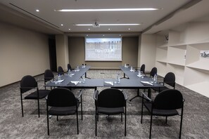 A conference room with a long table, black chairs, a projector screen, and a carpeted floor. - Grand Duka Hotel & Spa (Durrës)