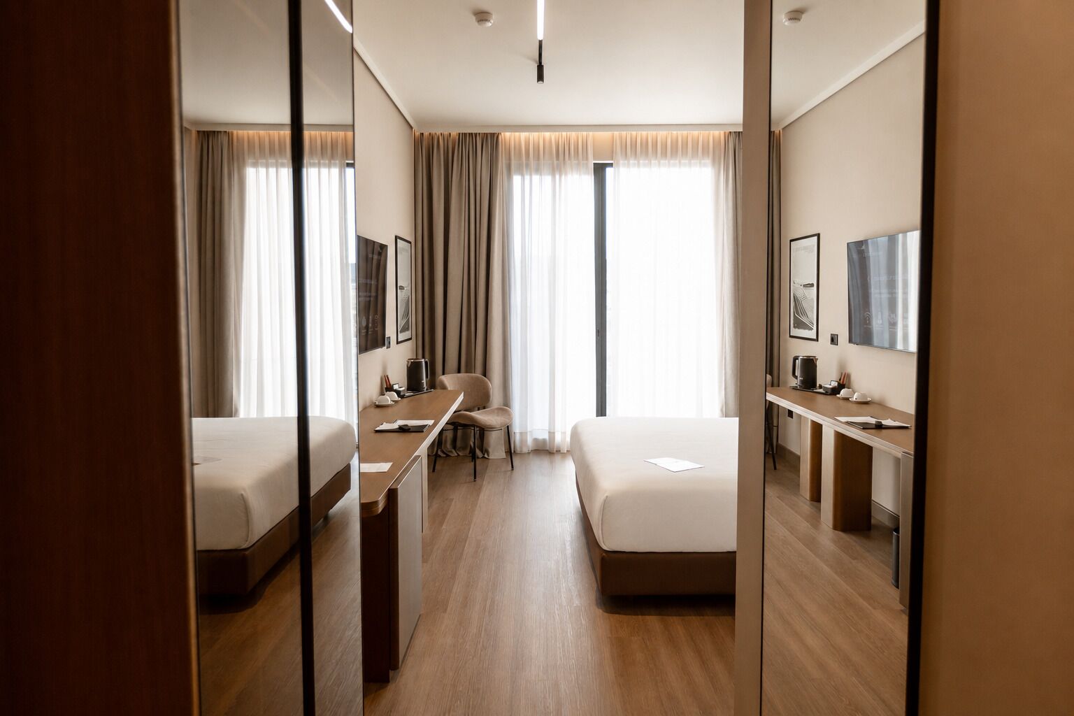 A hotel room with two beds, a desk, a chair, and a large mirror.