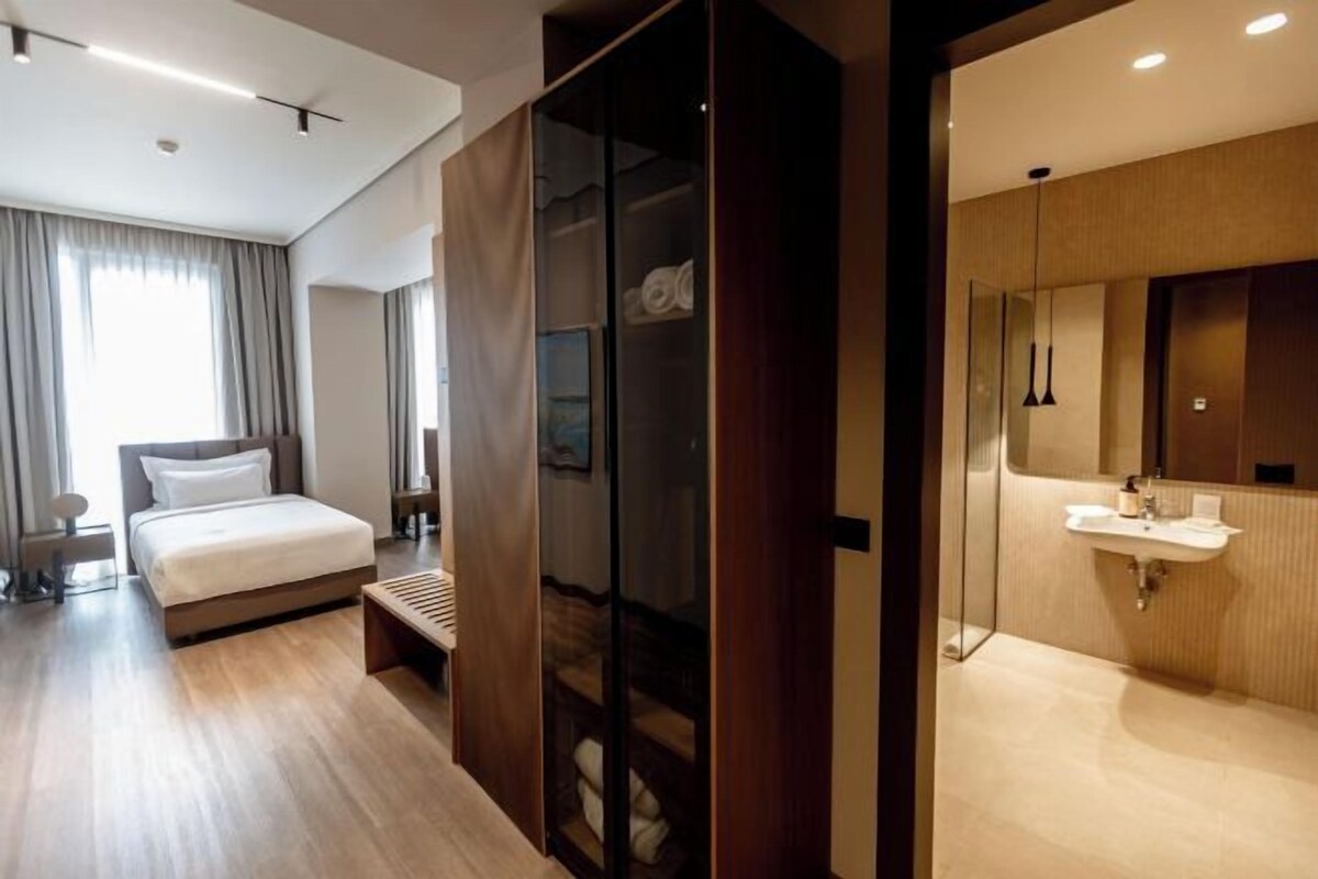 A modern hotel room with a bed, bedside table, and a bathroom with a sink and mirror.