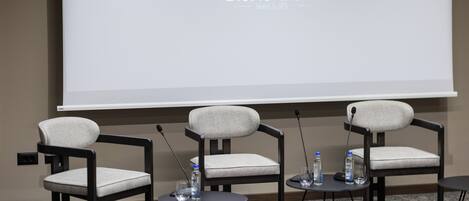 A conference room with three chairs, a projector screen displaying 'Grand Duka Hotel & Spa,' and water bottles on small tables.
