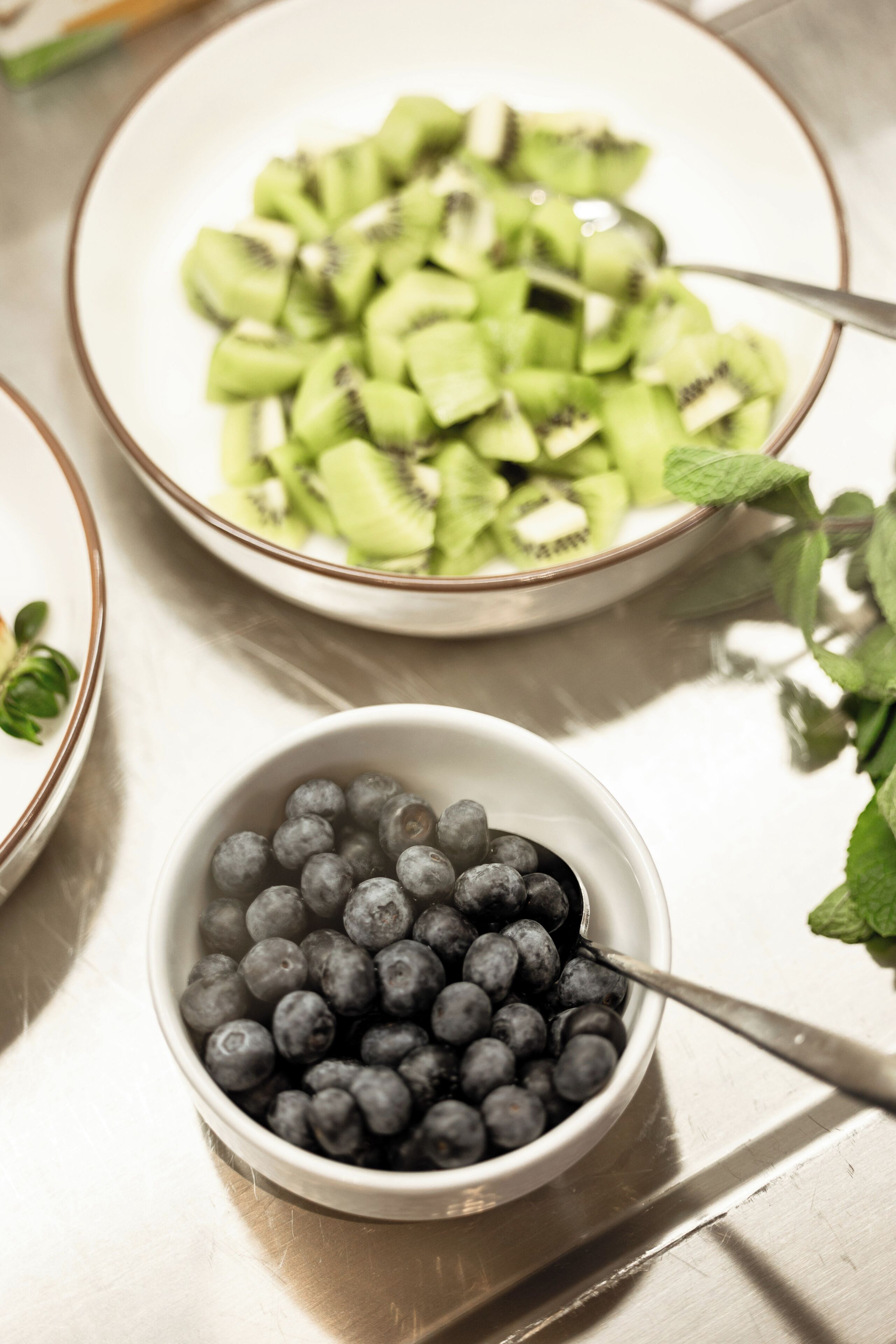 A bowl of blueberries and a bowl of sliced kiwi on a table.