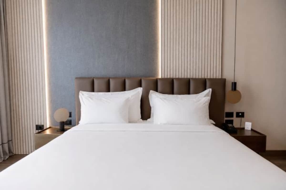 Una camera d'albergo con un letto grande, due comodini, una testiera e un tavolino con una lampada.