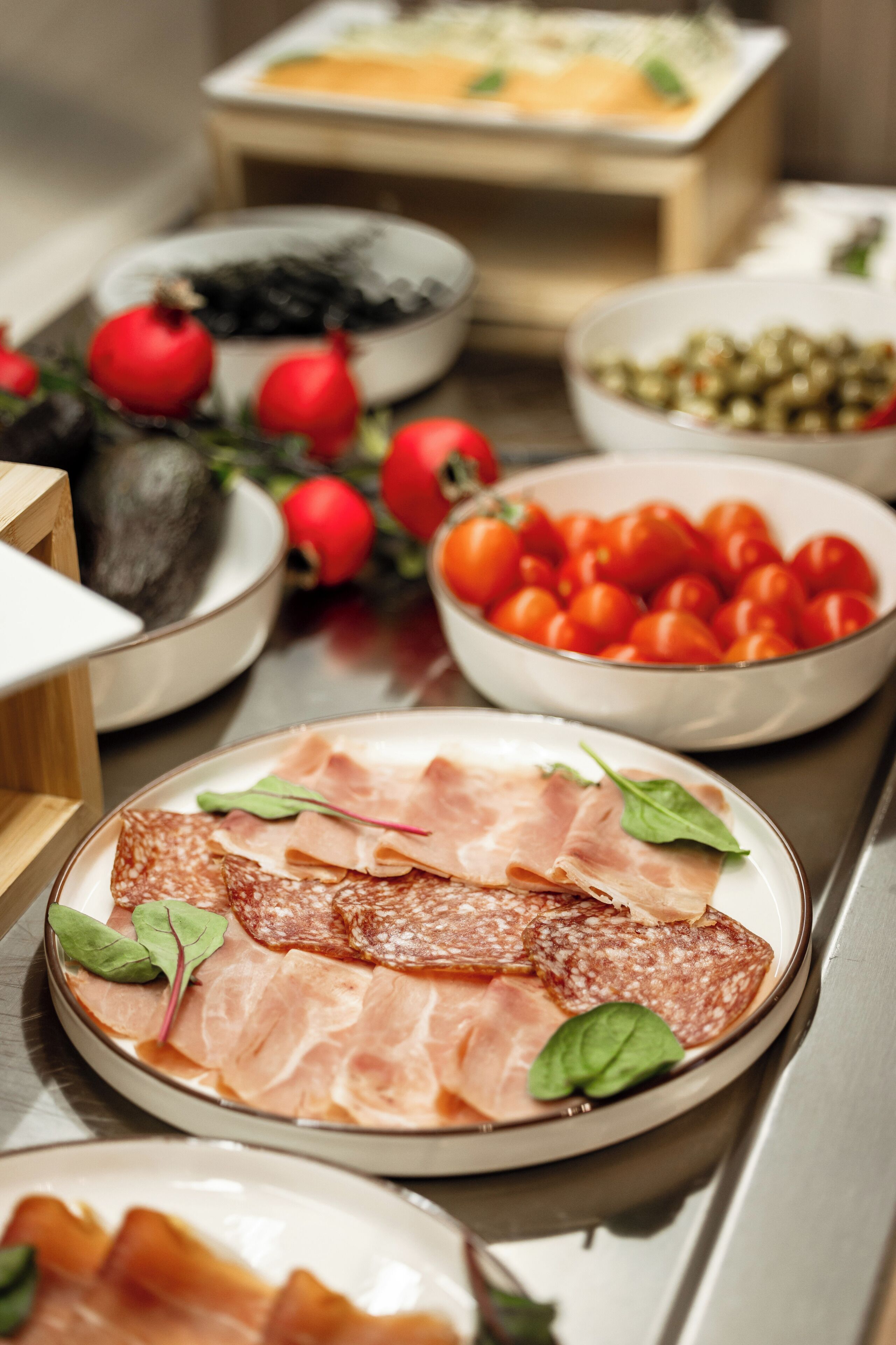 A table with various food items including sliced meats, tomatoes, olives, and a bowl of cherry tomatoes.