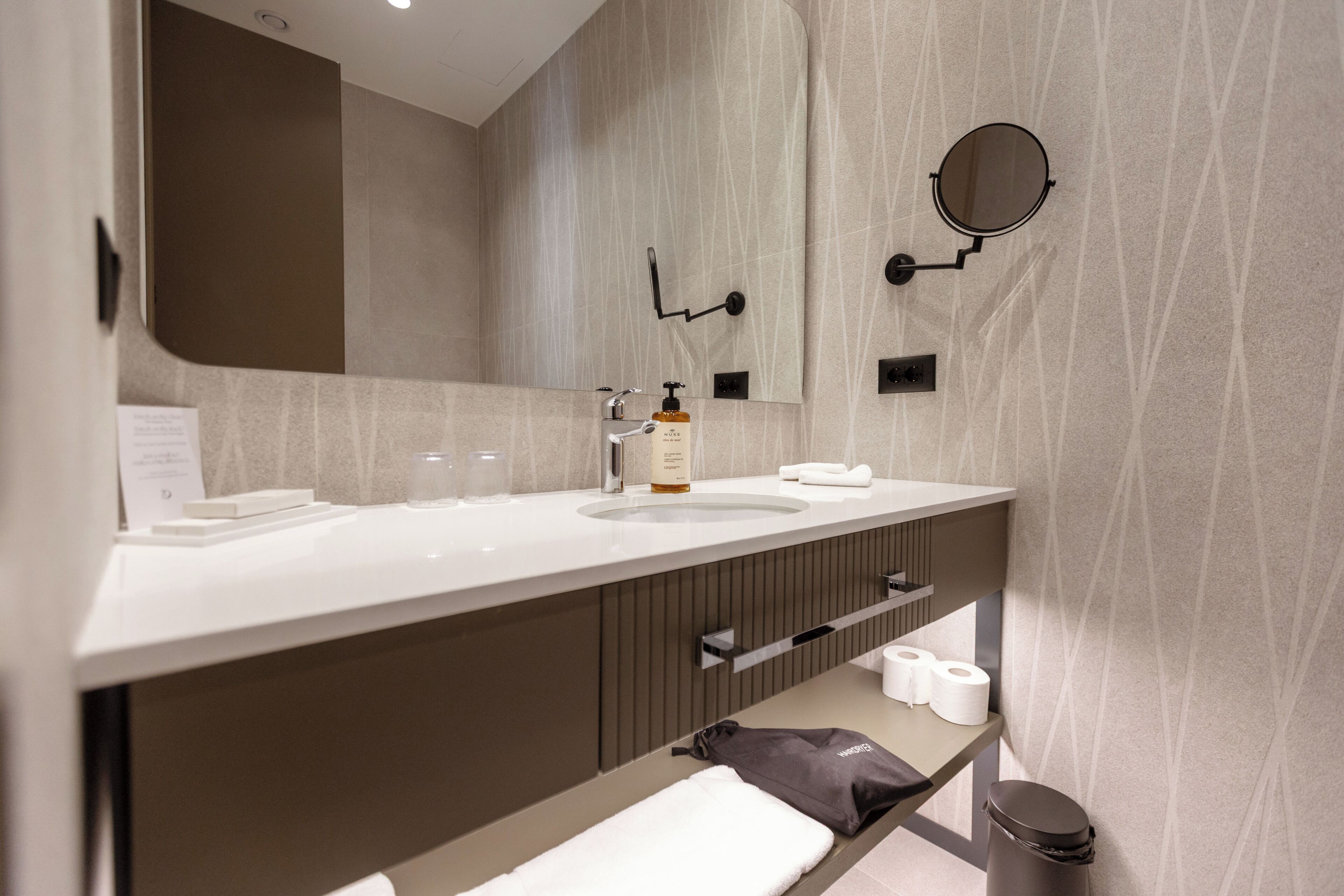 Une salle de bain moderne équipée d’un double lavabo, d’un miroir, d’un porte-serviettes et d’une poubelle.