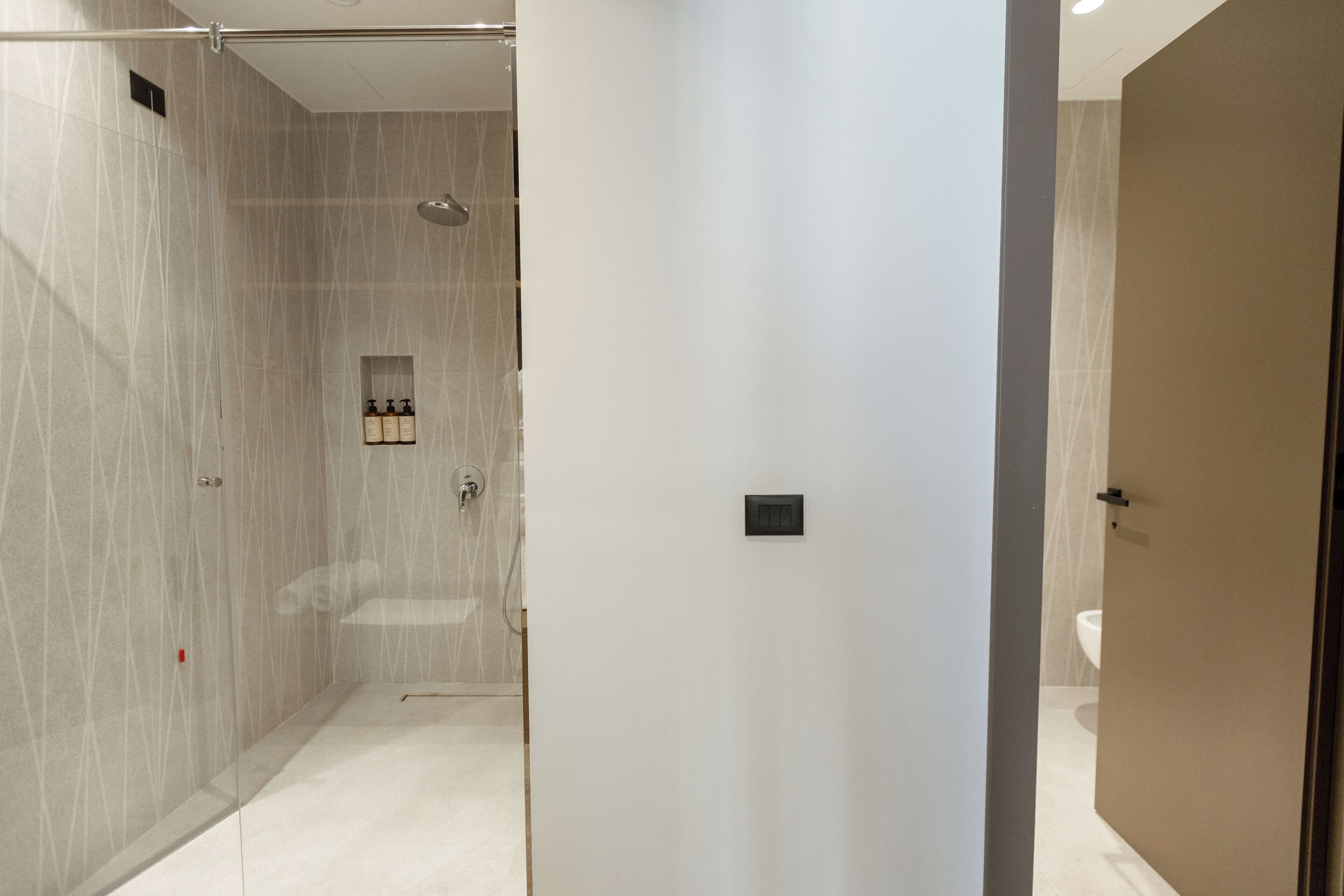 A modern bathroom with a glass shower enclosure, a small sink, and a toilet visible through an open door.